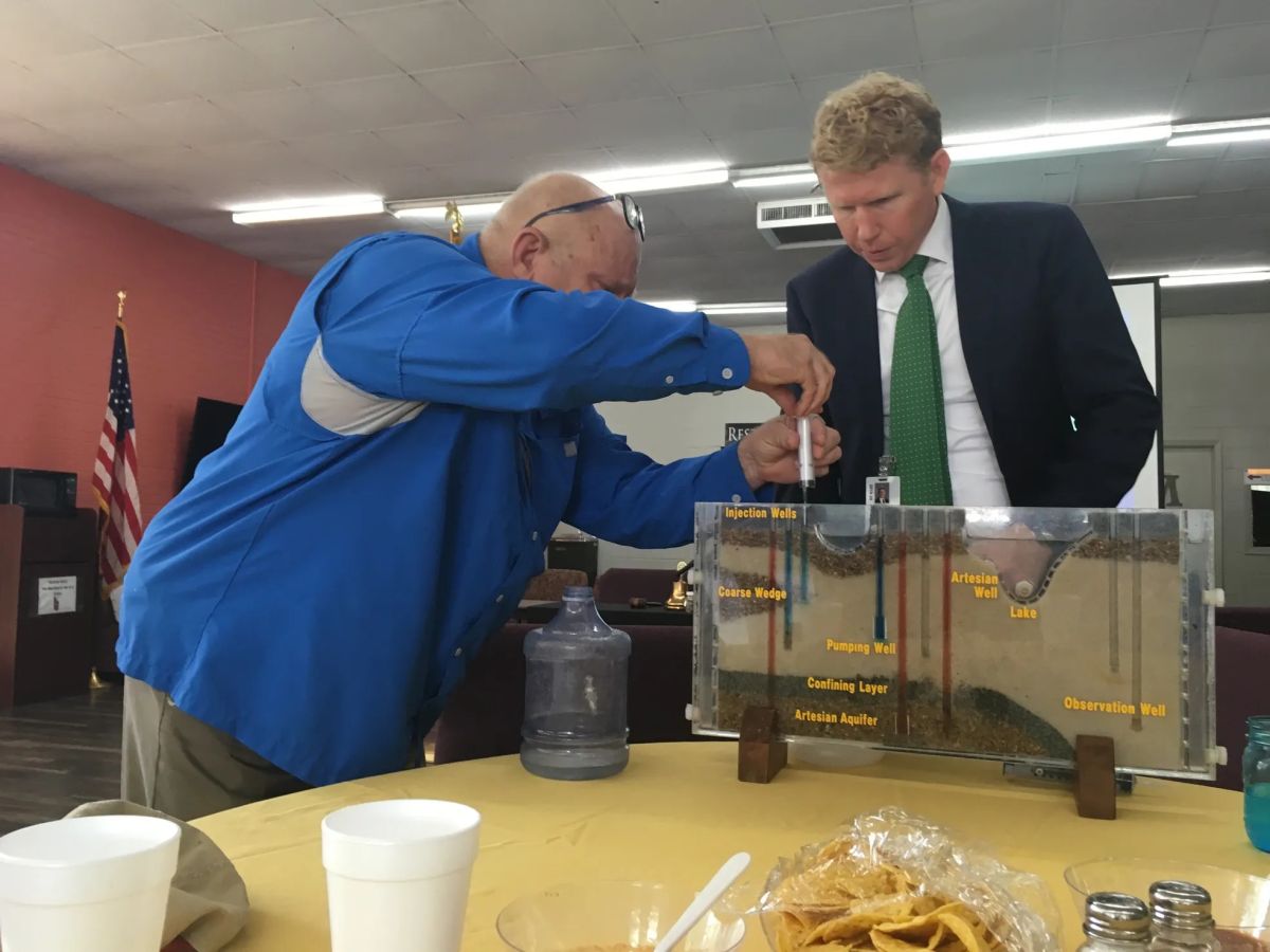 man in blue shirt at table demonstrating something with other person